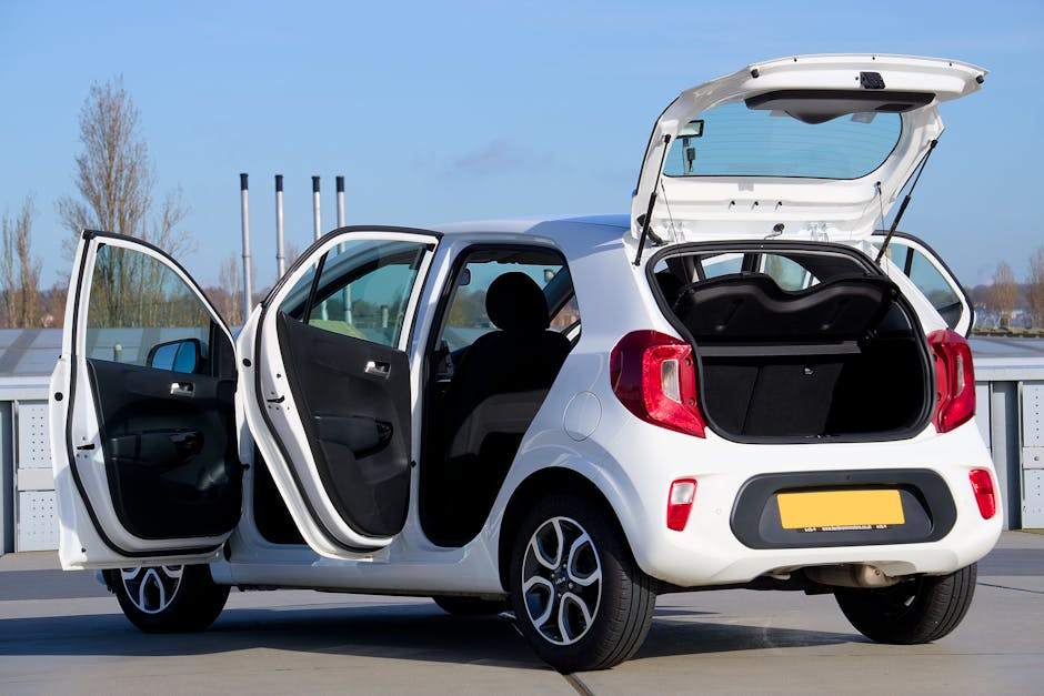 A white compact car with open doors and trunk, photographed in an urban outdoor setting.
