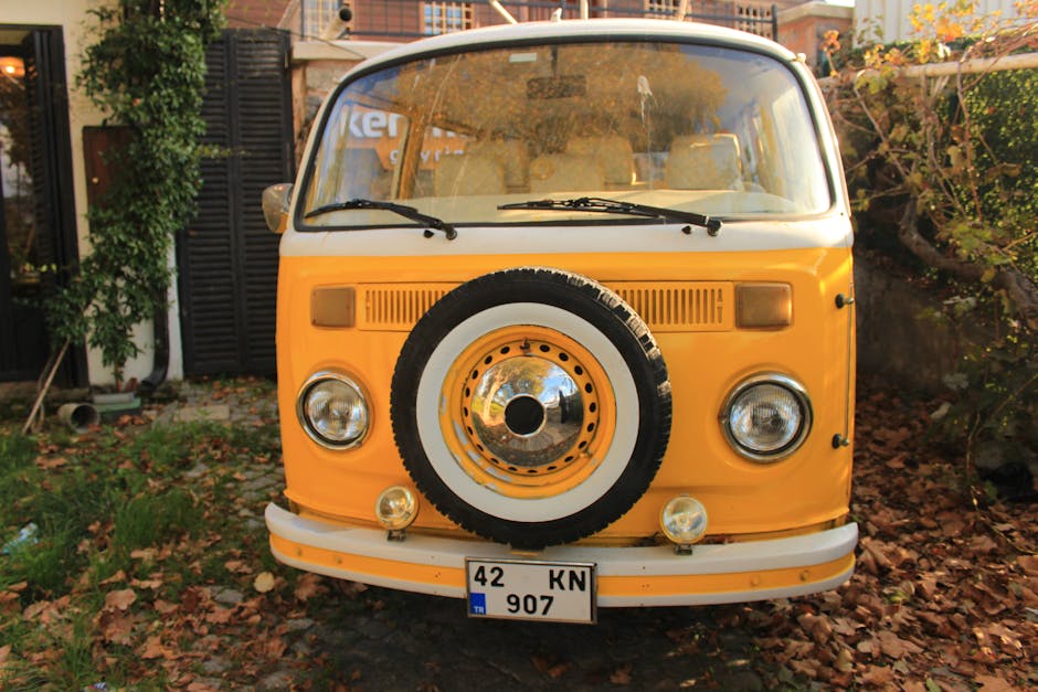 Front view of a classic yellow camper van parked among autumn leaves.