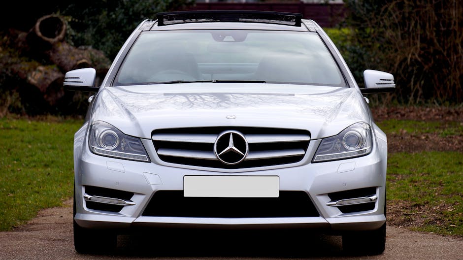Front view of a sleek silver luxury coupe car parked on a road, surrounded by greenery